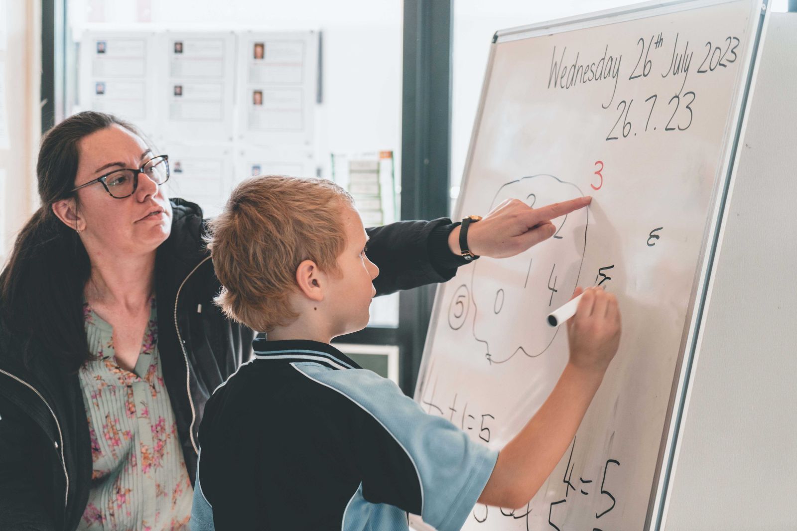 Teacher assisting student with a whiteboard math exercise